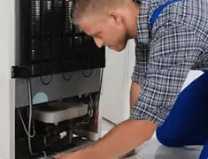 Refrigerator repair technician servicing the compressor and condenser area in Boston, MA
