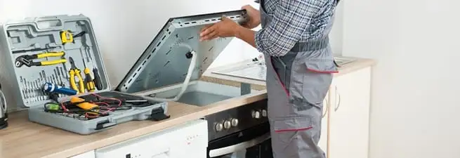 Cooktop repair technician lifting a built-in stovetop for service in Boston, MA
