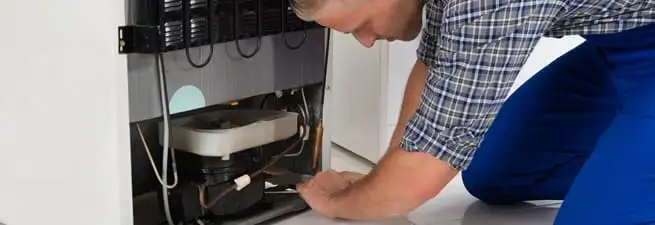 Refrigerator repair technician servicing the compressor and condenser area in Boston, MA