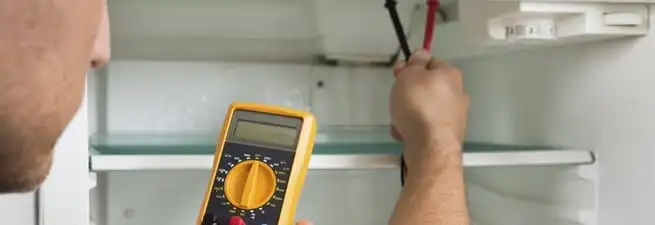 Refrigerator repair technician testing electrical components with a multimeter in Boston, MA